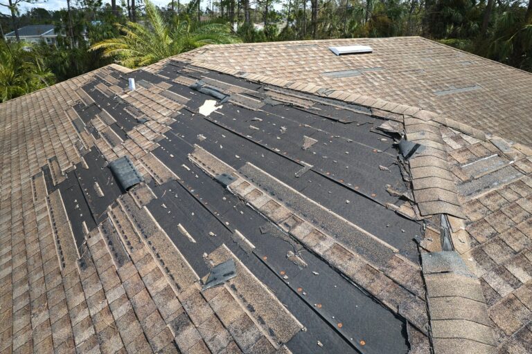 Wind damaged house roof with missing asphalt shingles after hurricane Ian in Florida.